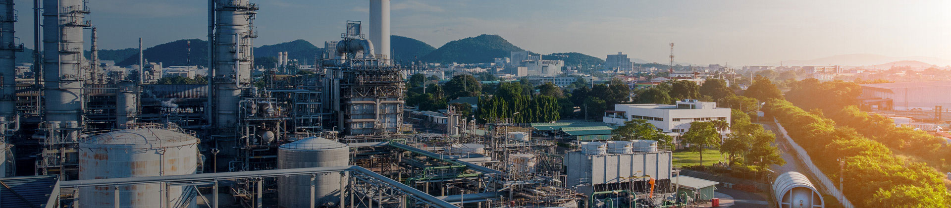 Sun setting on industrial plant with backdrop of mountains.