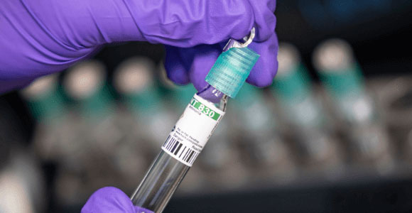 Purple-gloved hands holding a Hach TNTPlus Vial test reagent, which are incredibly simple to use and cut down on waste.